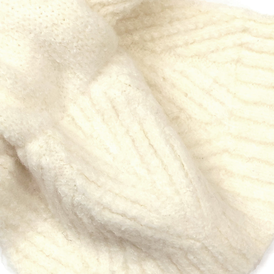 Close-up of the POM Charlotte cream pull-through scarf showing the soft, fluffy herringbone and cable knit texture in warm cream.