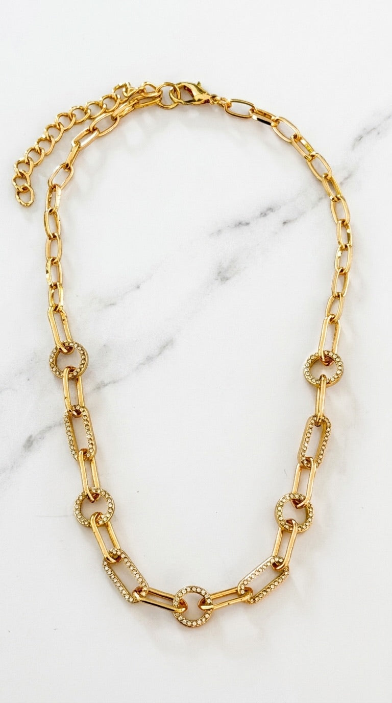 Envy gold chain necklace with alternating smooth rectangular links and textured circular links, displayed on a white marble background.