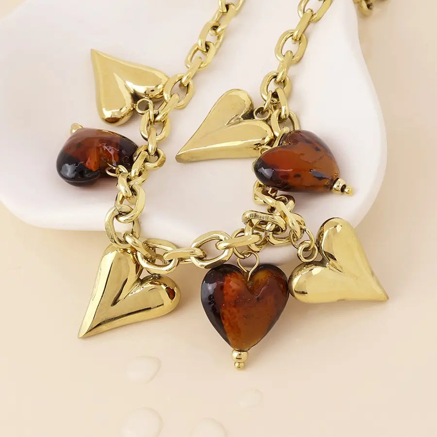 Gold-tone heart chain necklace with polished amber heart charms, displayed on a white dish against a light beige background.