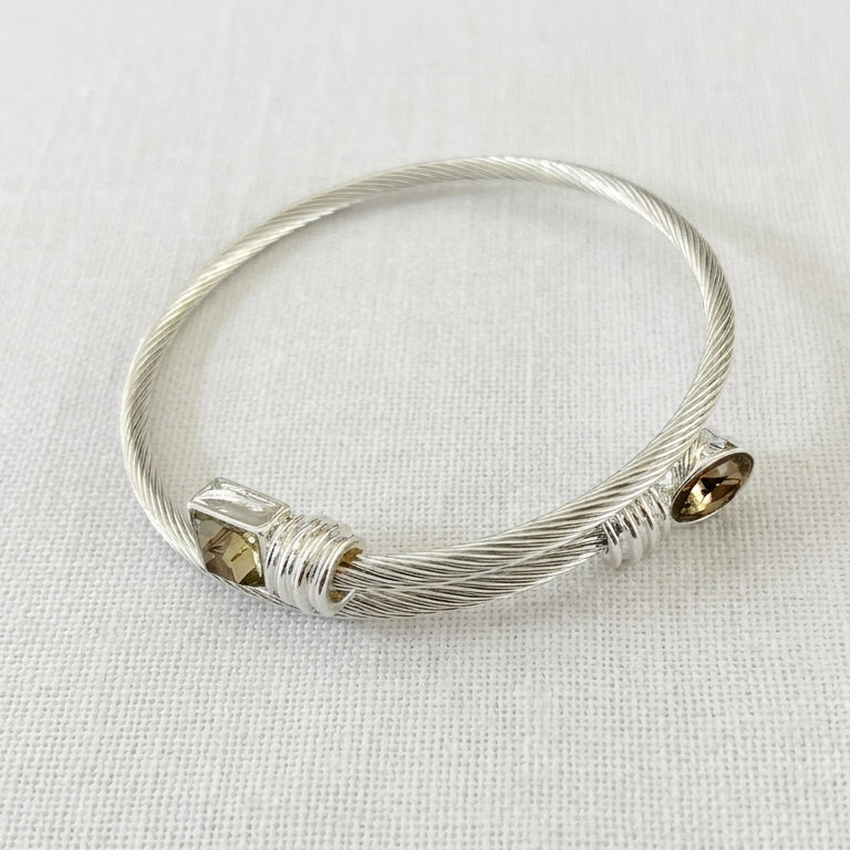 Envy silver twisted cable open bangle with square smoky crystal and round smoky crystal ends on cream linen background