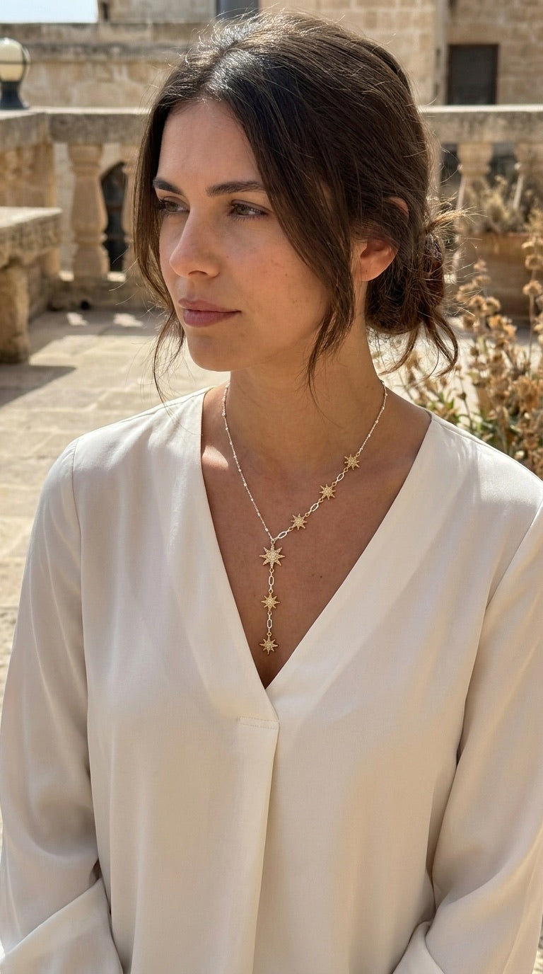 Model wearing Envy two-tone gold star lariat necklace with white v-neck blouse outdoors