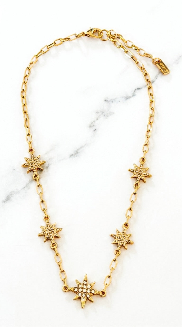 Envy gold oval link chain necklace with five pavé crystal star charms on marble background