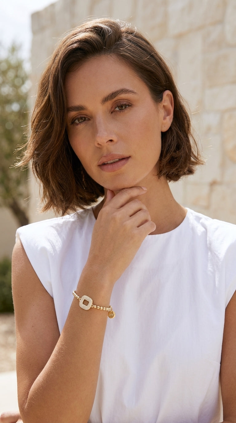 Model wearing Envy gold ball bead bracelet with pavé crystal open oval link with white sleeveless top
