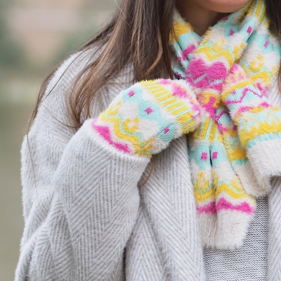 Model wearing POM Mia neon pattern fluffy knit wristwarmers with a matching Mia neon fair isle scarf, styled over a grey herringbone coat and grey knit jumper outdoors.