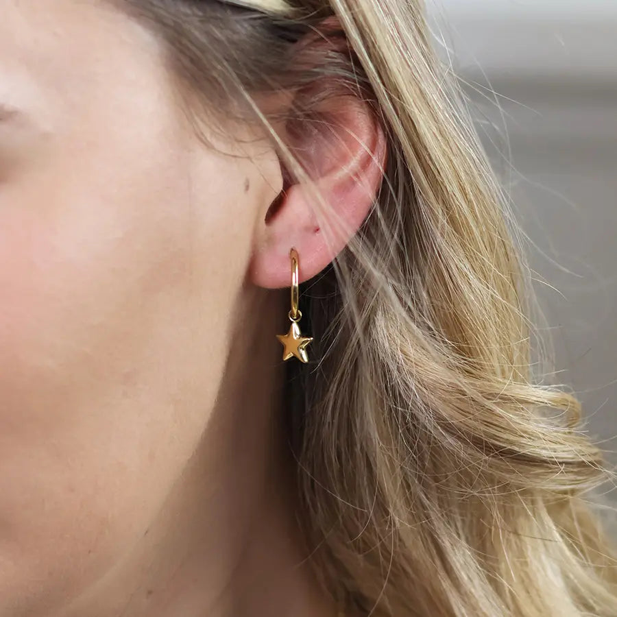 Close-up of model wearing POM Starlet gold star charm hoop earring, showing the delicate hoop and sculptural star pendant.