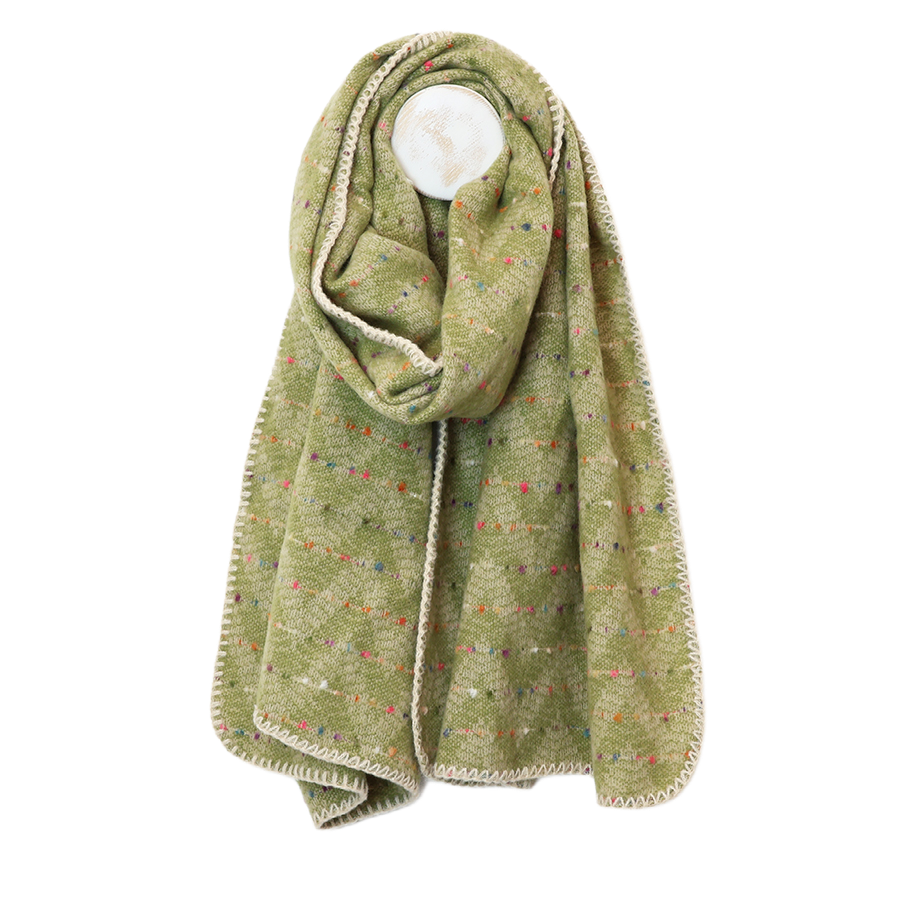 POM Tara pistachio green confetti fleck blanket wrap scarf draped on a mannequin stand against a white background, showing the soft pistachio green fabric with scattered multicolour confetti fleck and cream chevron blanket stitch edge.
