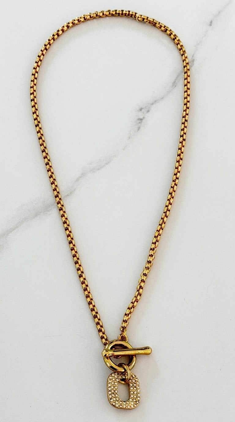 Envy chunky antique gold box chain necklace with front T-bar toggle clasp and pavé crystal rounded rectangle pendant on marble background