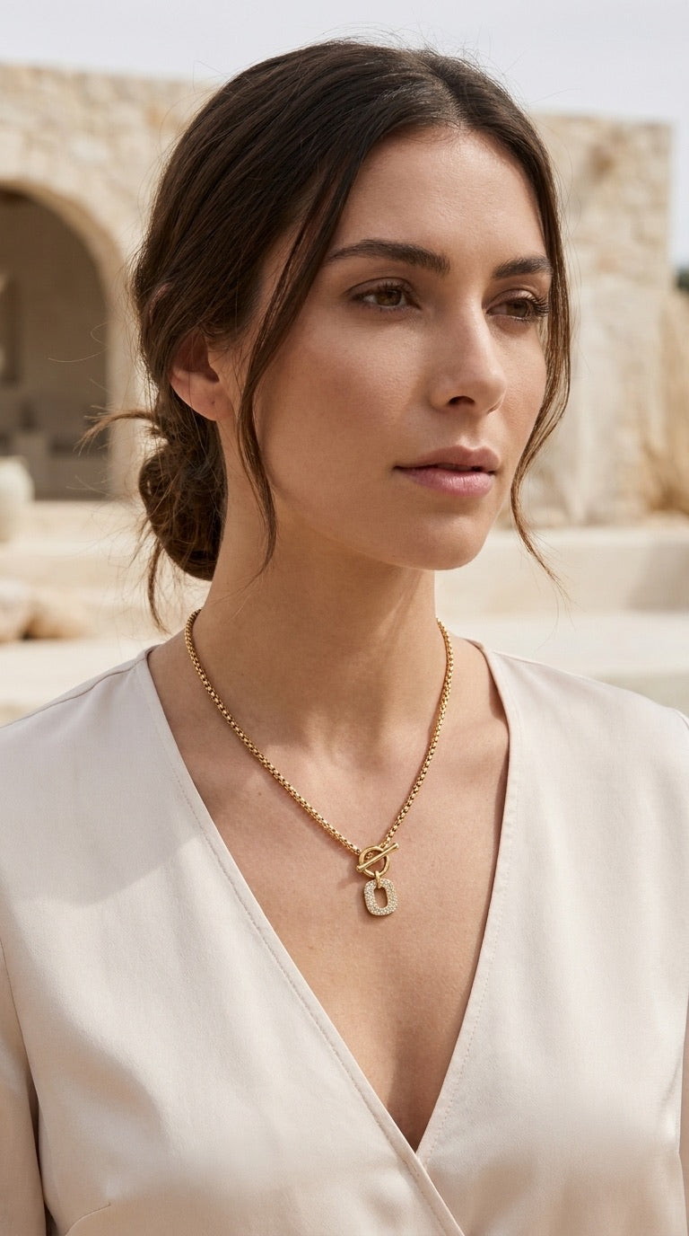 Model wearing Envy antique gold box chain T-bar necklace with pavé rectangle pendant with cream wrap top