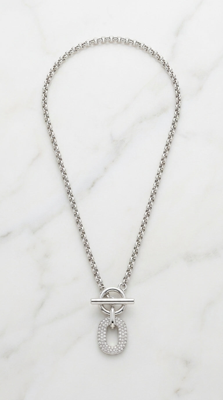 Envy chunky silver box chain necklace with front T-bar toggle clasp and fully pavé crystal oval pendant on marble background