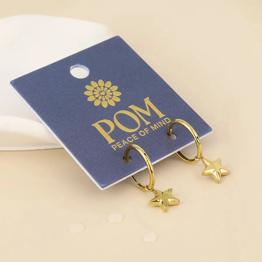POM Peace of Mind gold plated stainless steel star charm hoop earrings displayed on branded navy blue jewellery card against a beige background.