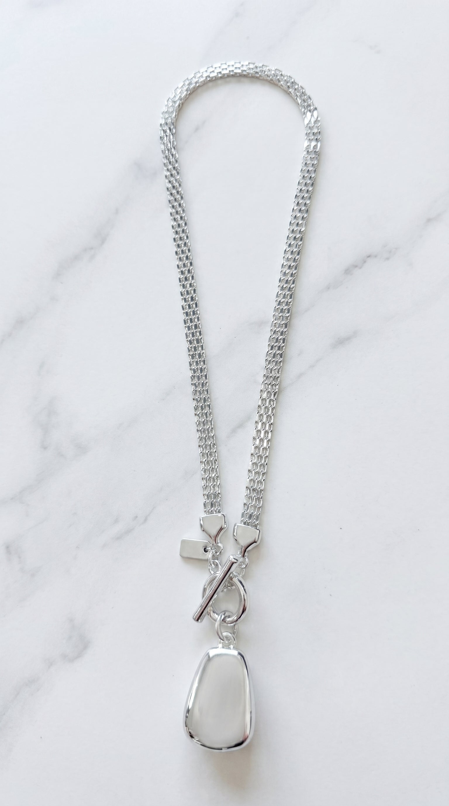 Envy silver double mesh chain necklace with front T-bar toggle clasp and polished silver organic pebble pendant on marble background