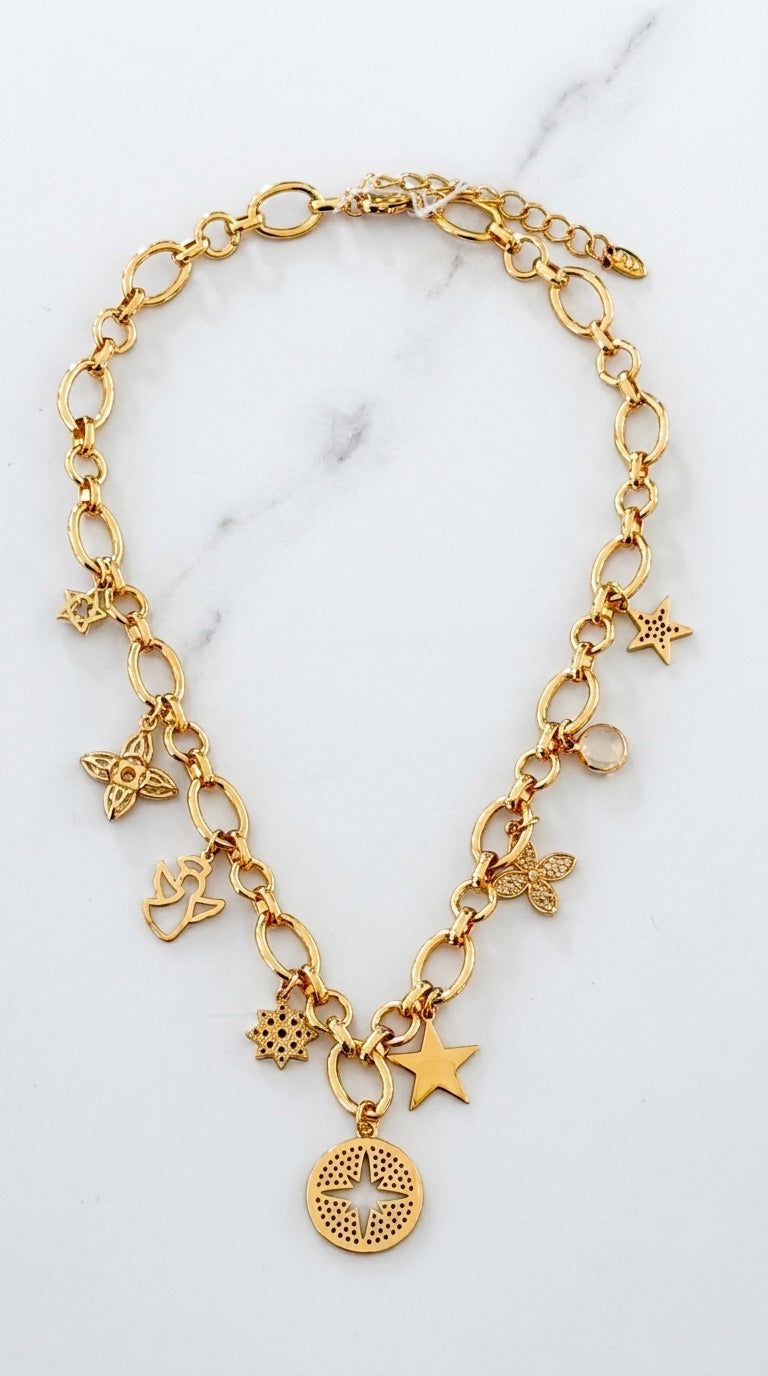 Envy chunky gold oval link chain necklace with nine mixed charms including stars, butterfly, snowflake, clover, bird and engraved compass disc pendant on marble background