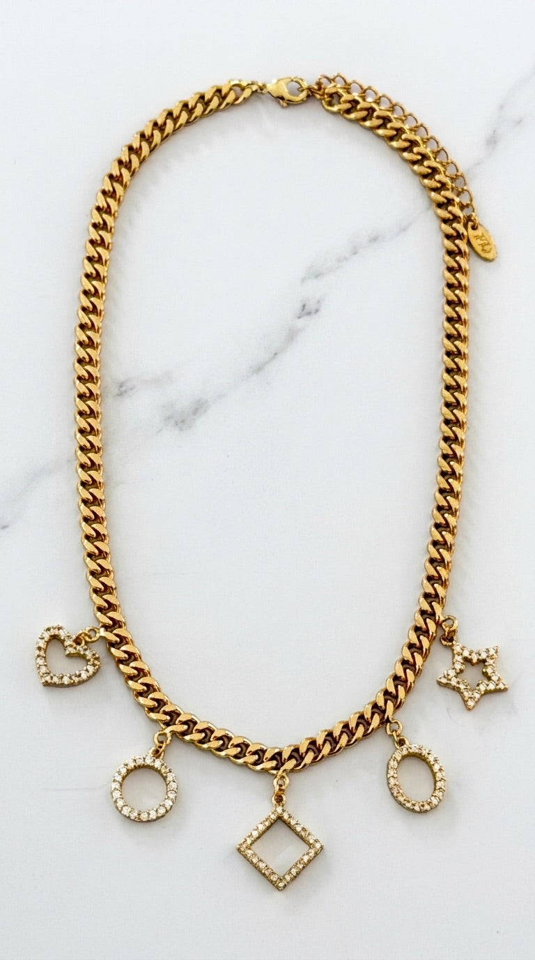Envy chunky gold curb chain necklace with five pavé crystal geometric charms — heart, circle, diamond, oval and star — on marble background
