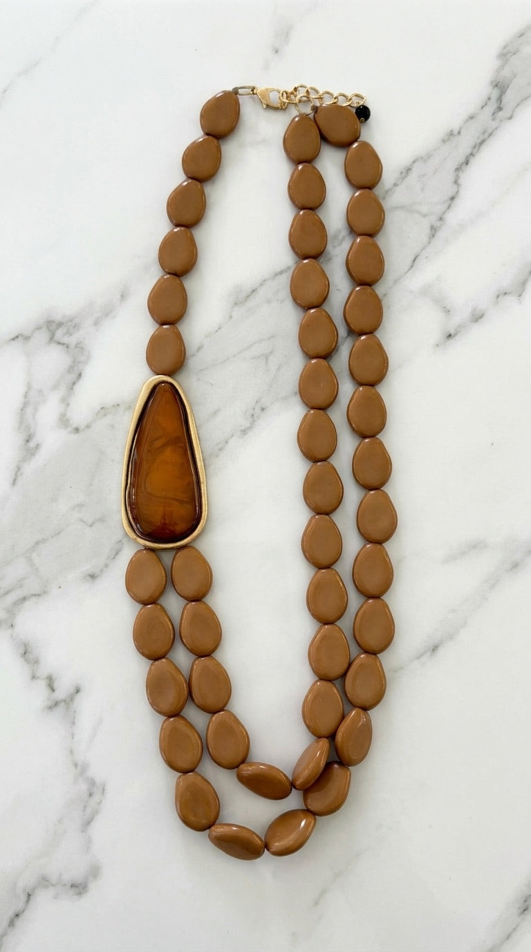 Envy double strand camel resin pebble bead necklace with gold-set amber teardrop pendant on marble background