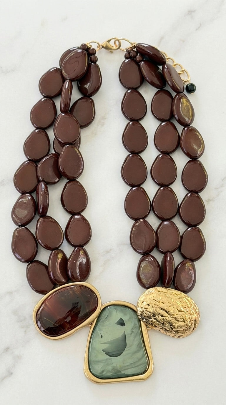 Envy double strand dark brown resin pebble bead necklace with green resin, amber stone and hammered gold disc pendant cluster on marble background