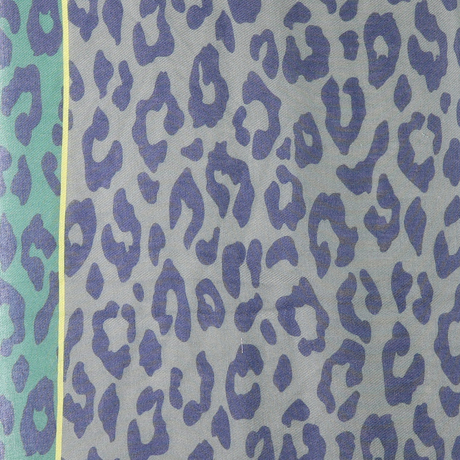 Close-up of the POM grey-green animal print recycled polyester scarf fabric, showing the oversized navy leopard print on the grey-blue ground with the teal reverse and neon yellow stripe border detail at the edge.