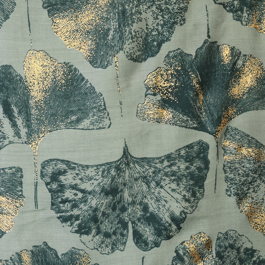 Close-up of the POM Greta sage mix ginkgo and metallic gold print scarf fabric, showing the oversized ginkgo leaves in deep teal with shimmering metallic gold detail on a soft sage green ground.