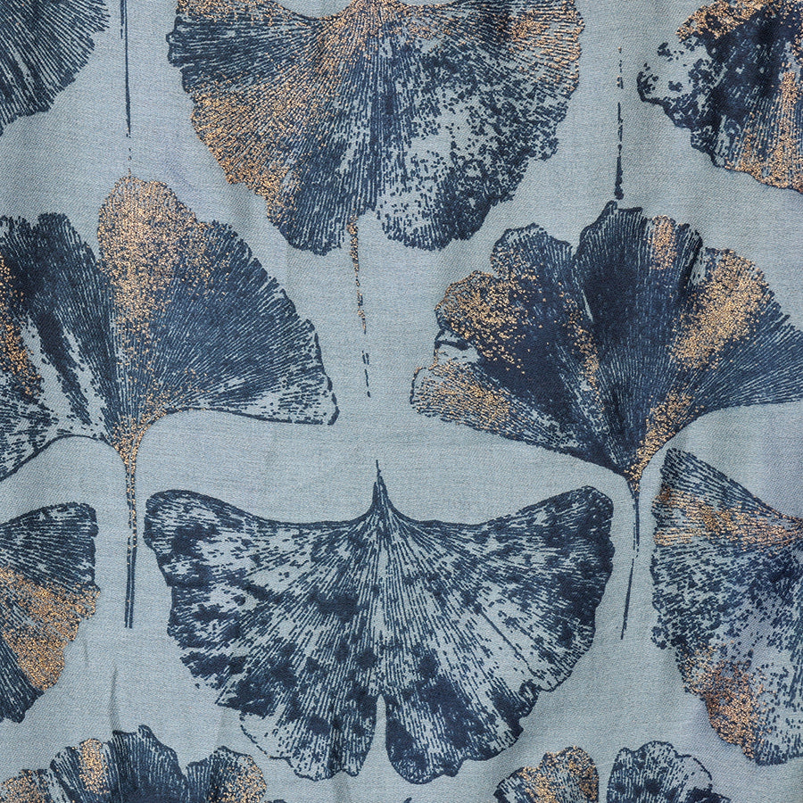 Close-up of the POM Greta blue mix ginkgo print scarf fabric, showing the oversized ginkgo leaves in deep navy and shimmering metallic gold on a soft slate blue ground.