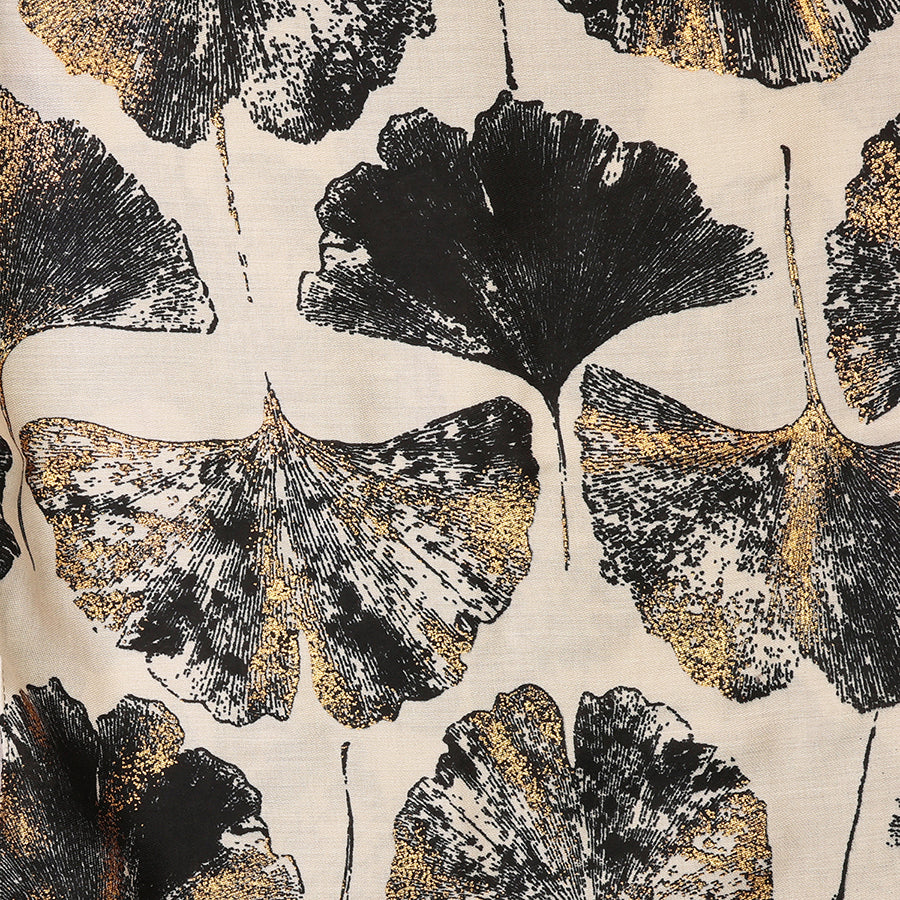 Close-up of the POM Greta natural mix ginkgo and metallic gold print scarf fabric, showing the oversized ginkgo leaves in deep black and shimmering metallic gold on a warm natural ecru ground.