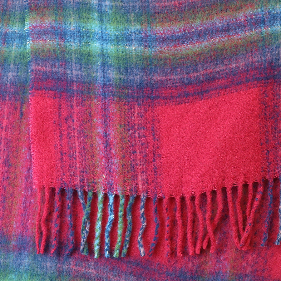 Close-up of the POM Miranda blue, green and raspberry mix scarf fabric, showing the bold oversized check in raspberry red, teal blue, sage green and purple with a soft blended finish and multicolour twisted fringe ends at the bottom edge.