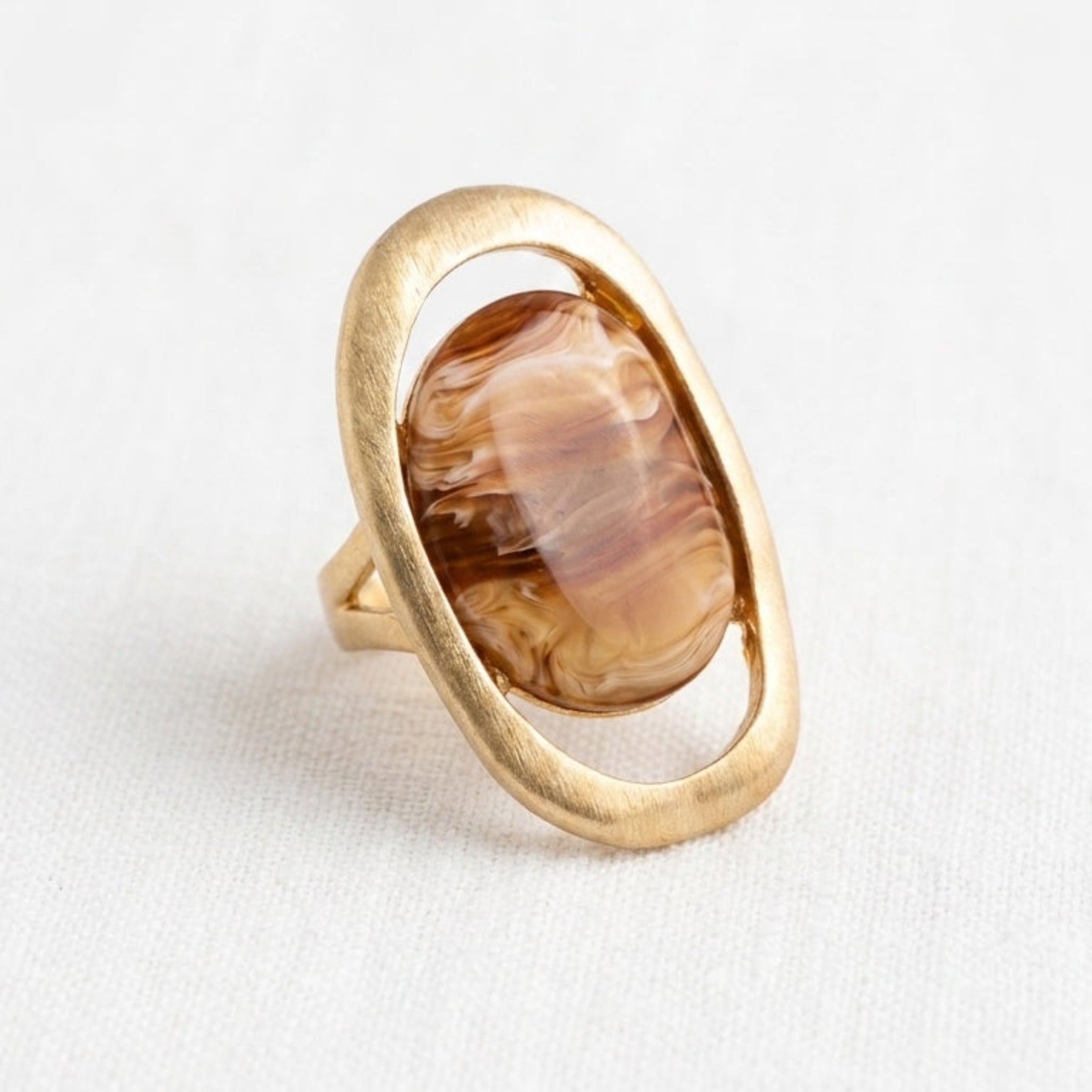 Envy gold ring featuring an open oval design that frames a large, polished brown agate stone, set against a clean white background.