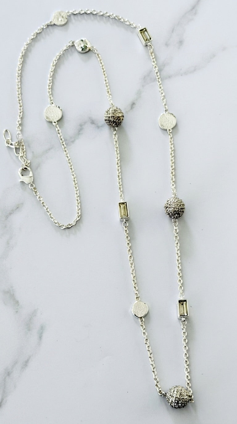 Envy long silver rolo chain necklace with pavé crystal ball, baguette, and disc stations on marble background