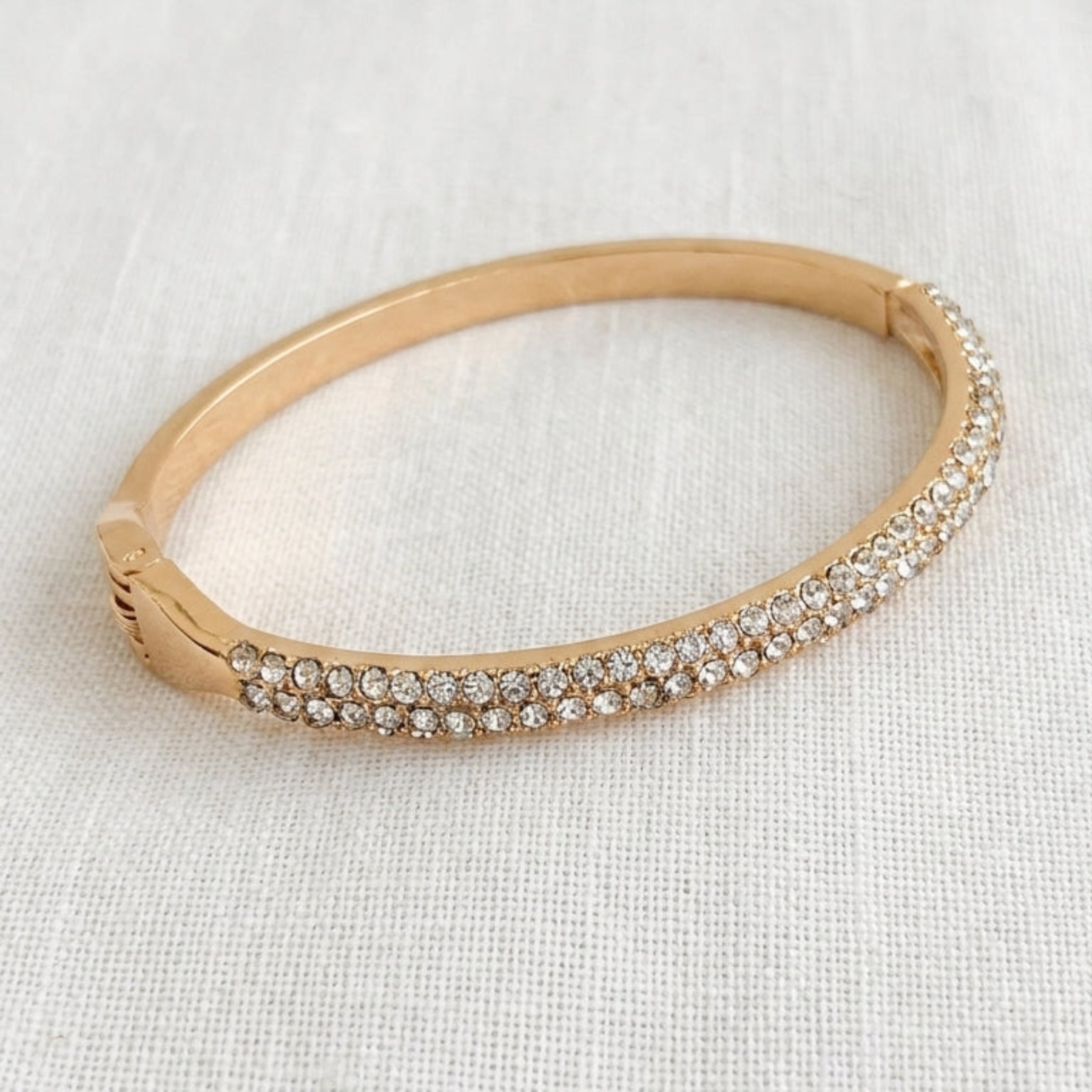 Envy gold hinged bangle with double row pavé crystal front on cream linen background