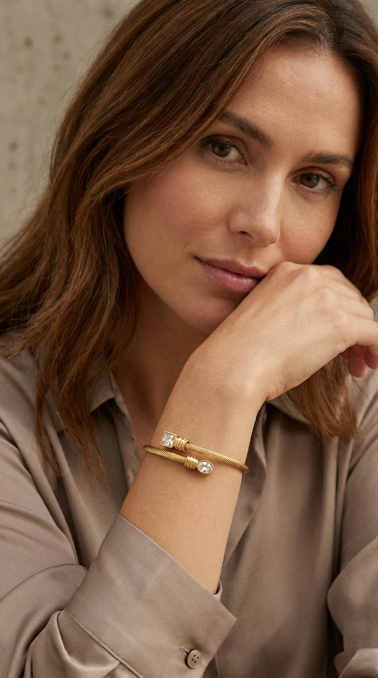 Model wearing Envy gold twisted cable bangle with square and round crystal ends with taupe satin shirt