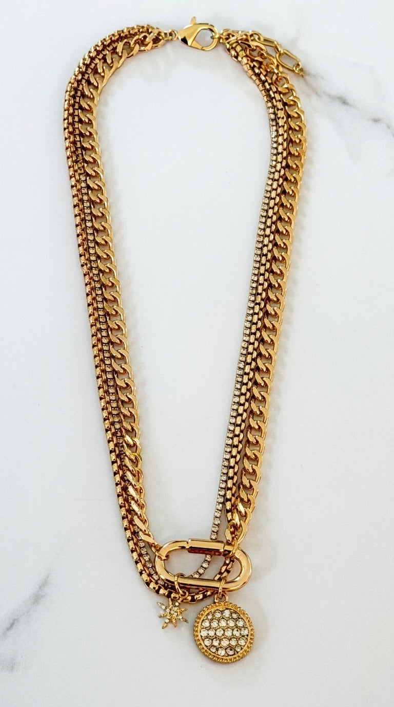 Envy gold layered curb chain and crystal tennis chain necklace with pavé carabiner, disc pendant and star charm on marble background
