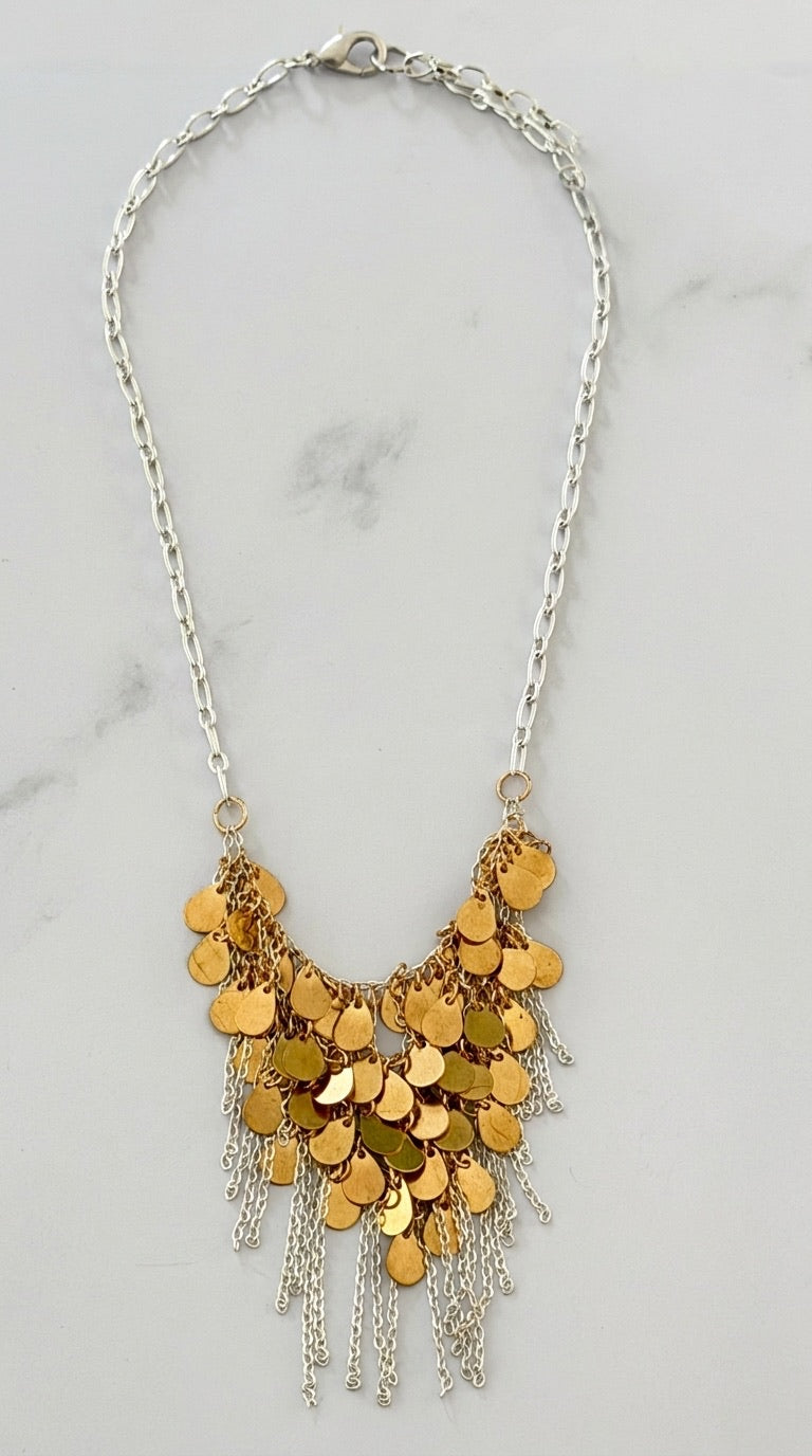 Envy two-tone bib necklace with layered gold coin discs and silver fringe chains on marble background
