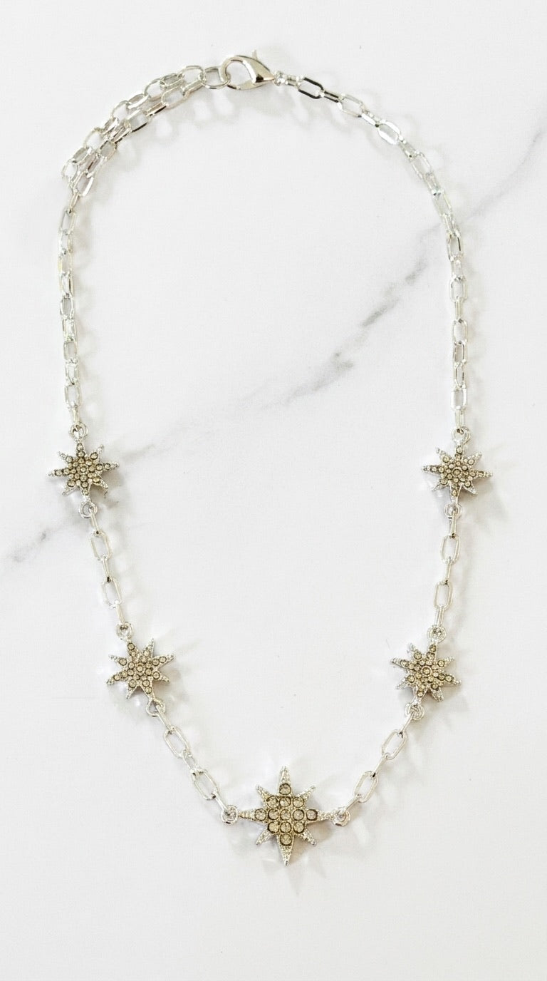 Envy silver oval link chain necklace with five pavé crystal star charms on marble background