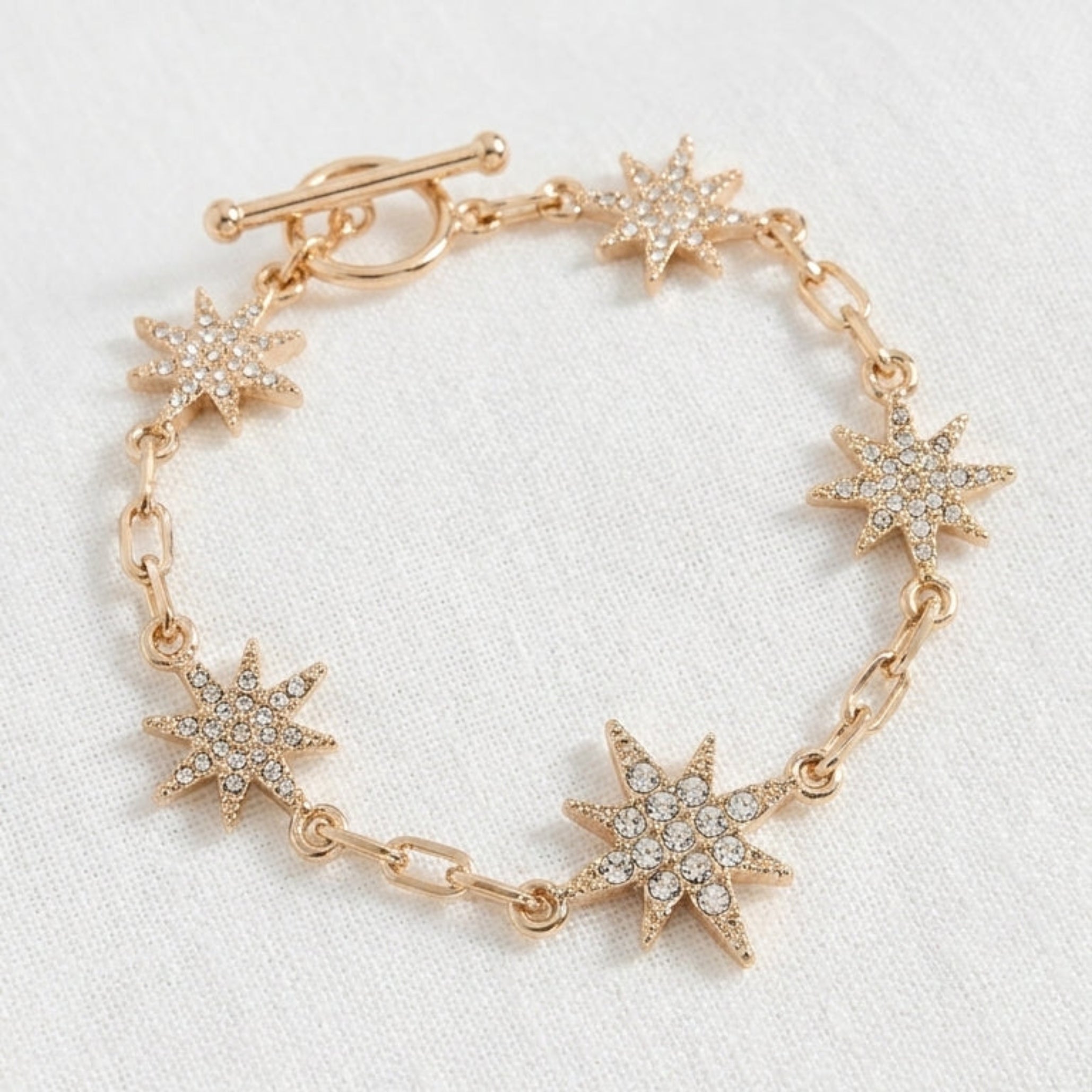 Envy gold paperclip chain bracelet with six fully pavé crystal eight-pointed star charms and T-bar toggle clasp on white background