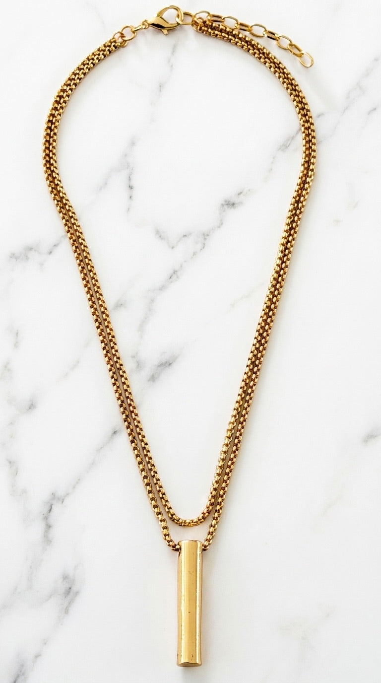Envy gold double-layer box chain necklace with cylindrical bar pendant on marble background