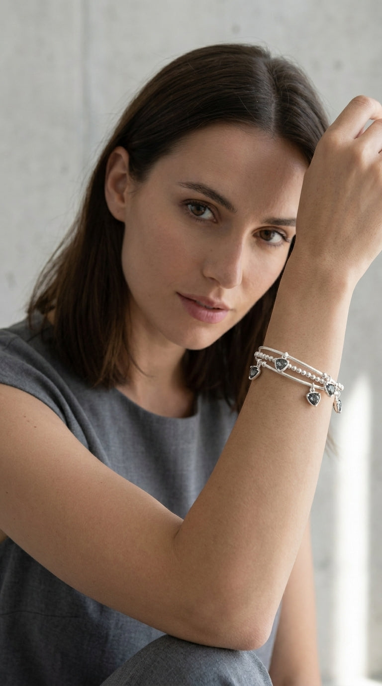 Model wearing Envy silver triple wrap bracelet with smoky trillion crystal drop charms with grey sleeveless top