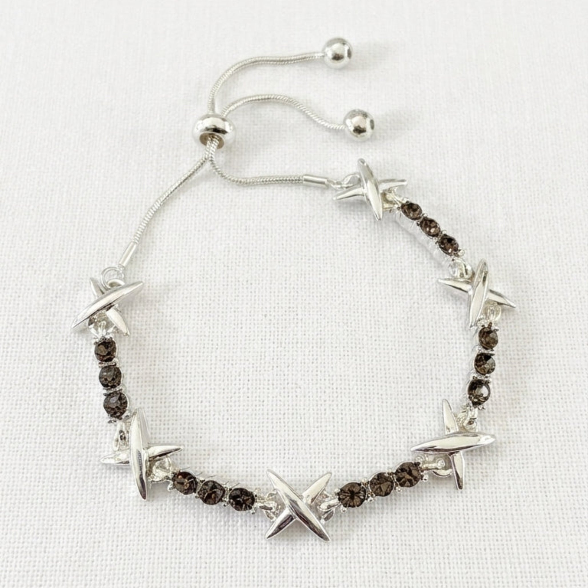 Envy silver adjustable slider bracelet with alternating four-pointed star charms and smoky grey crystals on cream linen background