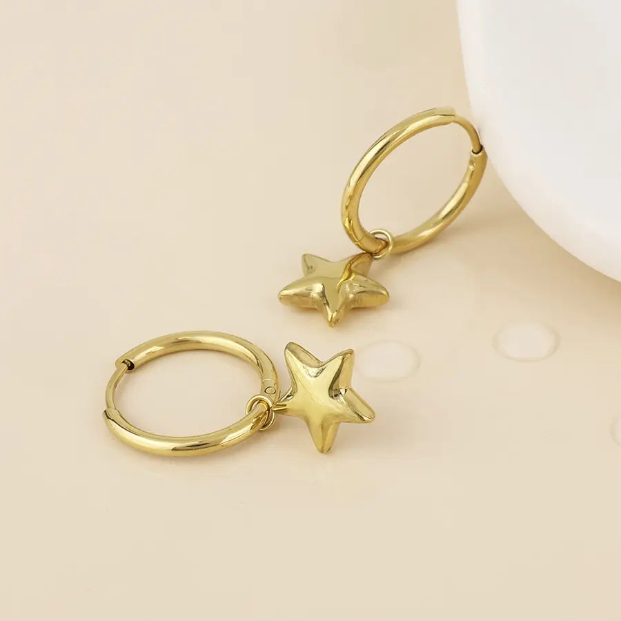 Pair of POM Starlet 14k gold plated stainless steel hoop earrings with polished 3D star charms, laid flat against a cream background.