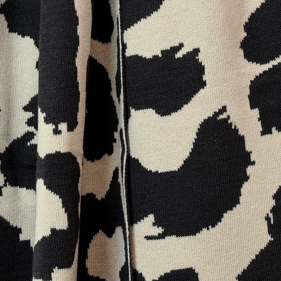 Close-up of the POM Carly oatmeal and black animal print knitted scarf fabric, showing the bold oversized leopard print pattern and soft fine knit texture.