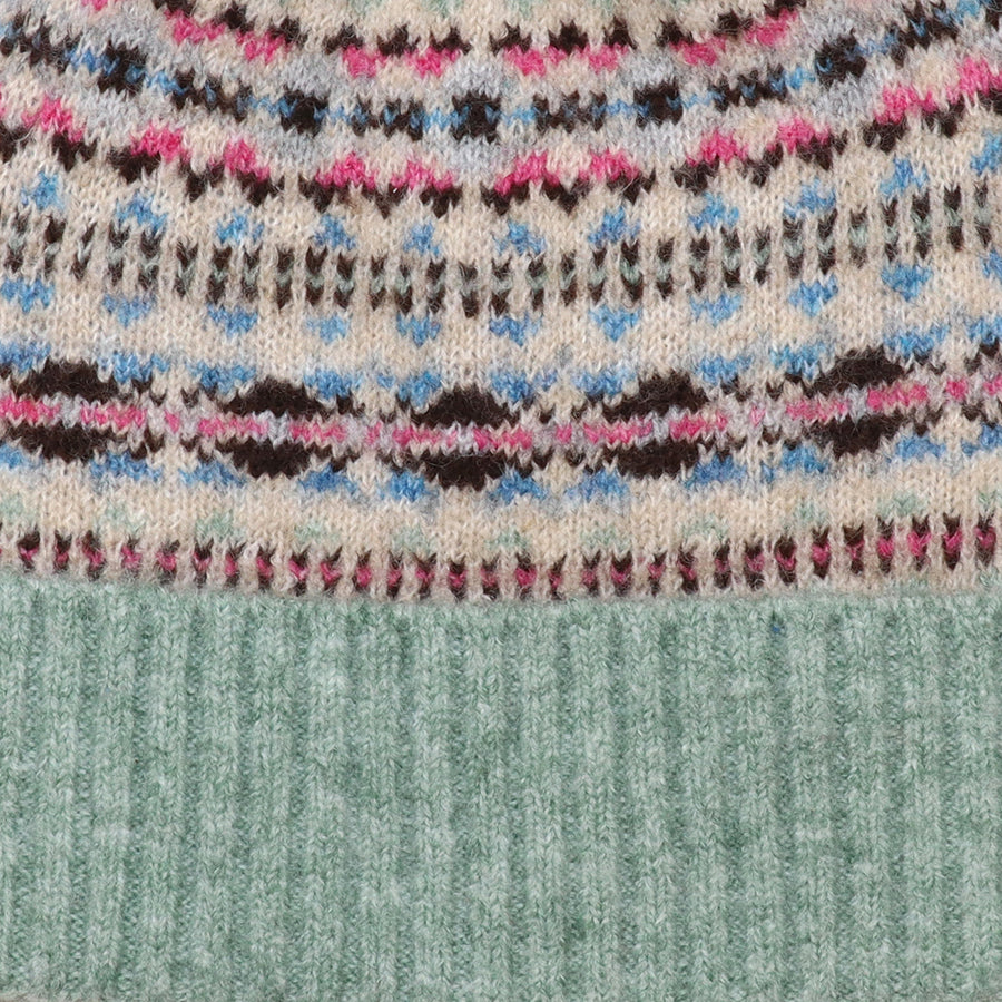 Close-up of the POM Iris bobble hat fabric, showing the intricate fair isle knit pattern in pink, blue, brown and oatmeal with the mint ribbed brim detail.