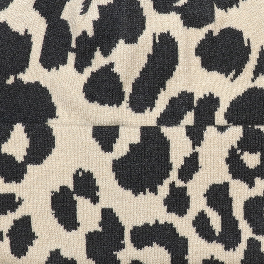 Close-up of the POM Carly oatmeal and black animal print beanie knit fabric, showing the bold oversized leopard print pattern and soft fine knit texture with ribbed cuff detail.