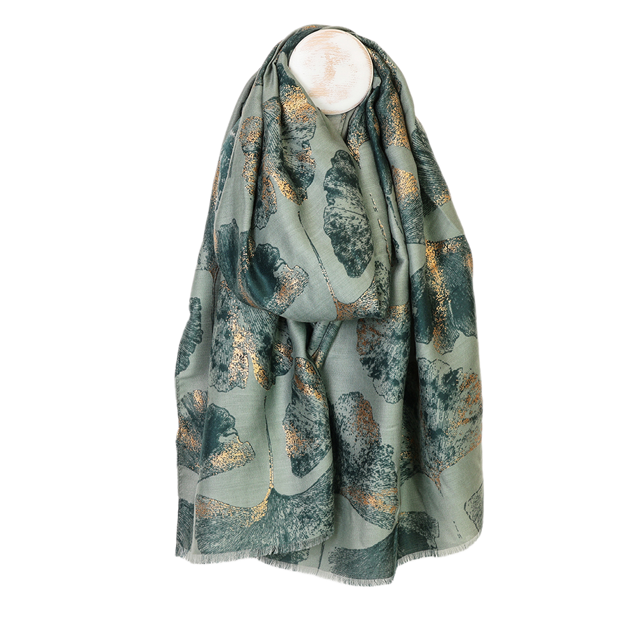 POM Greta sage mix ginkgo and metallic gold print scarf looped on a mannequin stand against a white background, showing the oversized deep teal and shimmering metallic gold ginkgo leaf print on a soft sage green ground with delicate fringe edge.