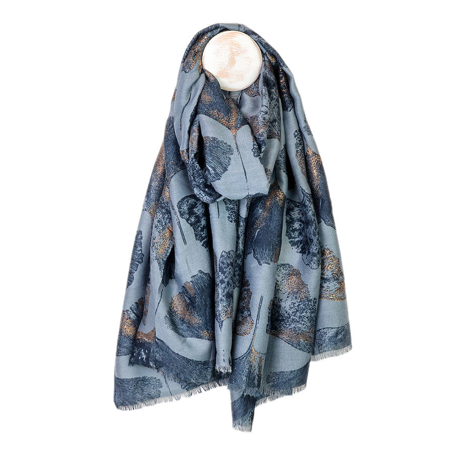 POM Greta slate blue ginkgo and metallic gold print scarf draped on a mannequin stand against a white background, showing the oversized navy and gold ginkgo leaf print all over with a delicate fringe edge.