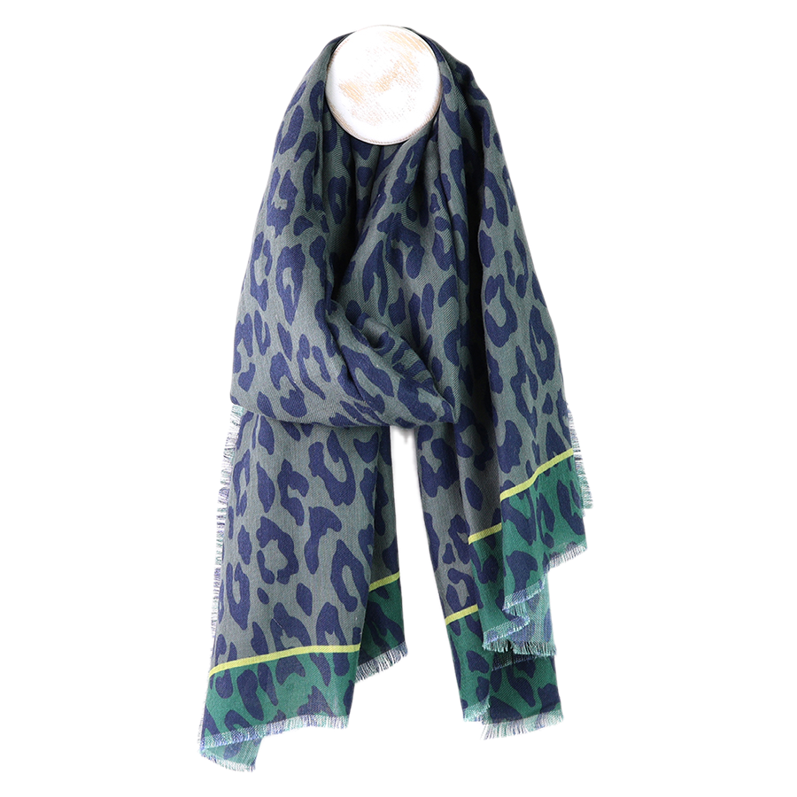 POM grey-green animal print recycled polyester scarf draped on a mannequin stand against a white background, showing the oversized navy leopard print on a grey-blue base with teal reverse and neon yellow stripe border at the ends with fringe edge.