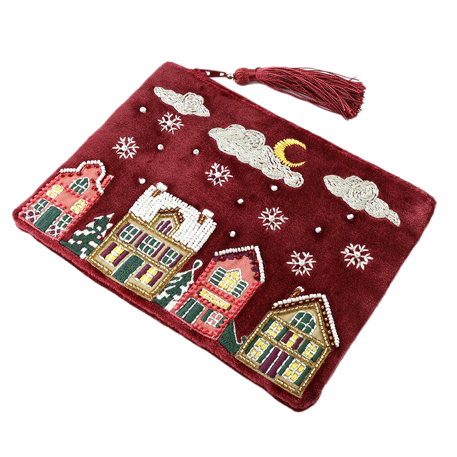 POM Winter Street wine velvet clutch purse with hand-embroidered and beaded winter village scene featuring snow-dusted houses, snowflakes and a crescent moon, with a tassel zip pull, shown against a white background.