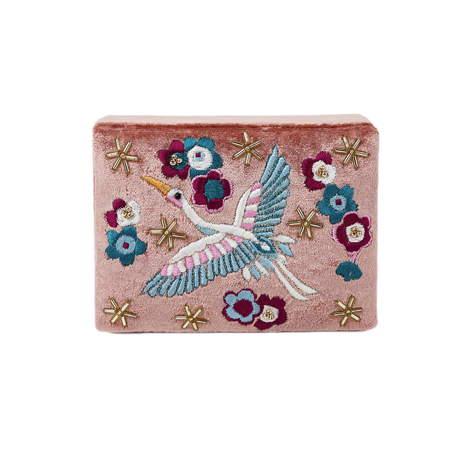 POM Crane blush velvet jewellery box shown from the front, hand-embroidered on the lid with a soaring crane in teal, white and pink, surrounded by teal and burgundy blooms and scattered gold star beads on soft blush velvet.